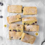 Lemon Blueberry Snack Cake sliced with powdered sugar, fresh flowers, blueberries, and a glass of milk