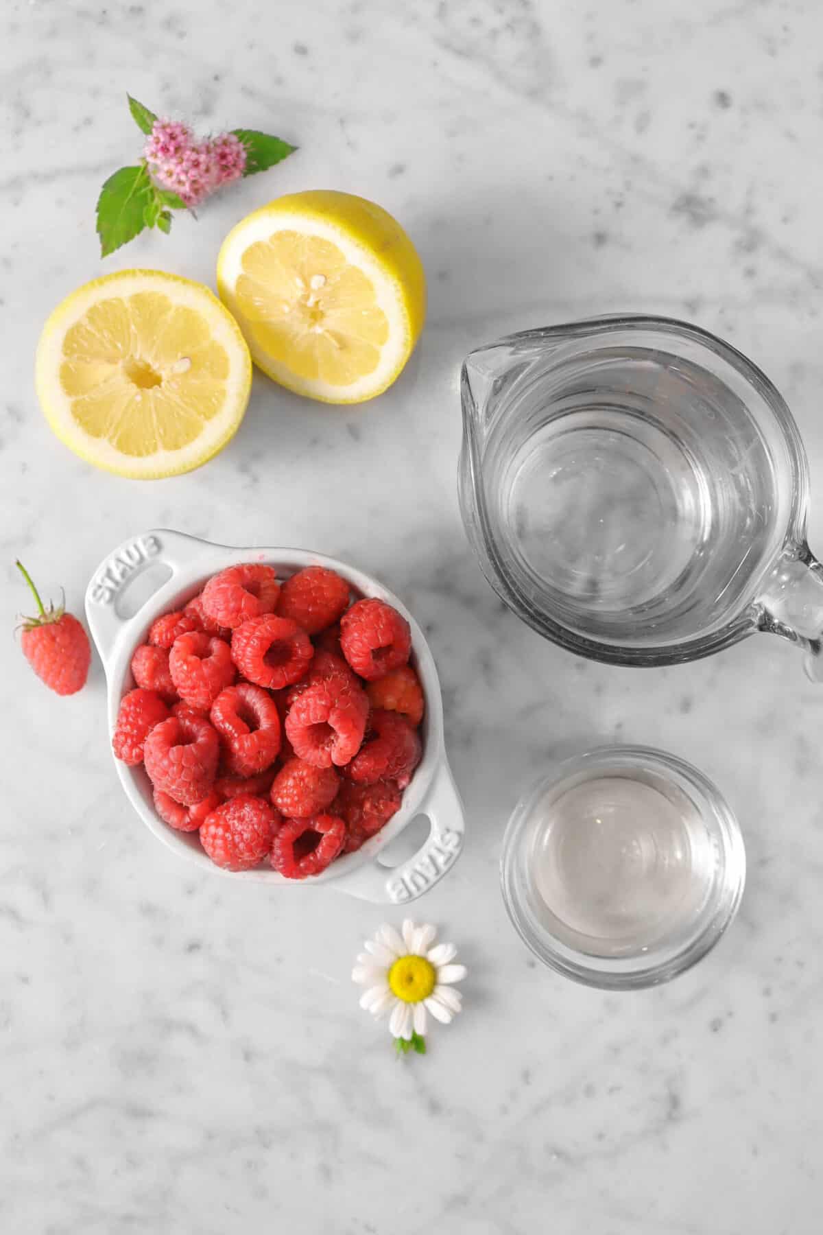 raspberries, a lemon sliced in half, a cup of water, simple syrup, and flowers