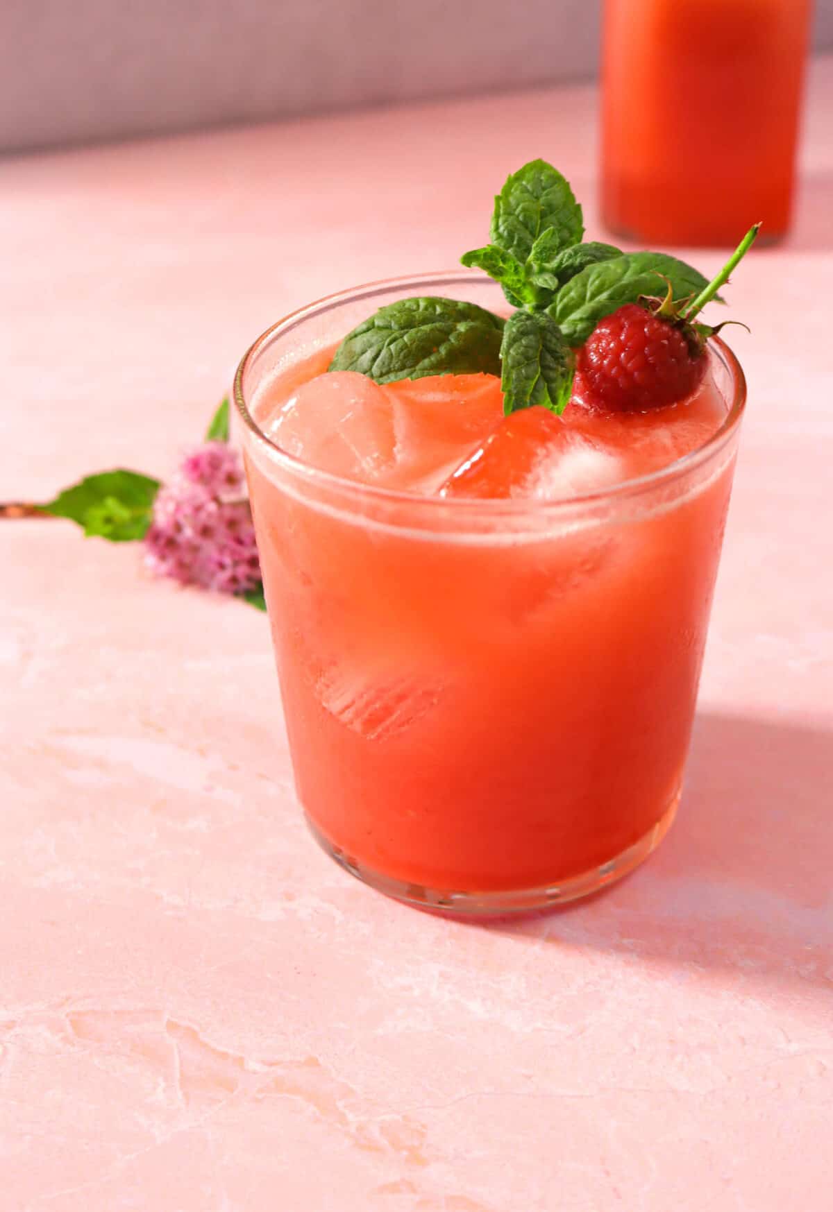 raspberry lemonade on a pink board with a raspberry, a mint sprig, and a jar of lemonade