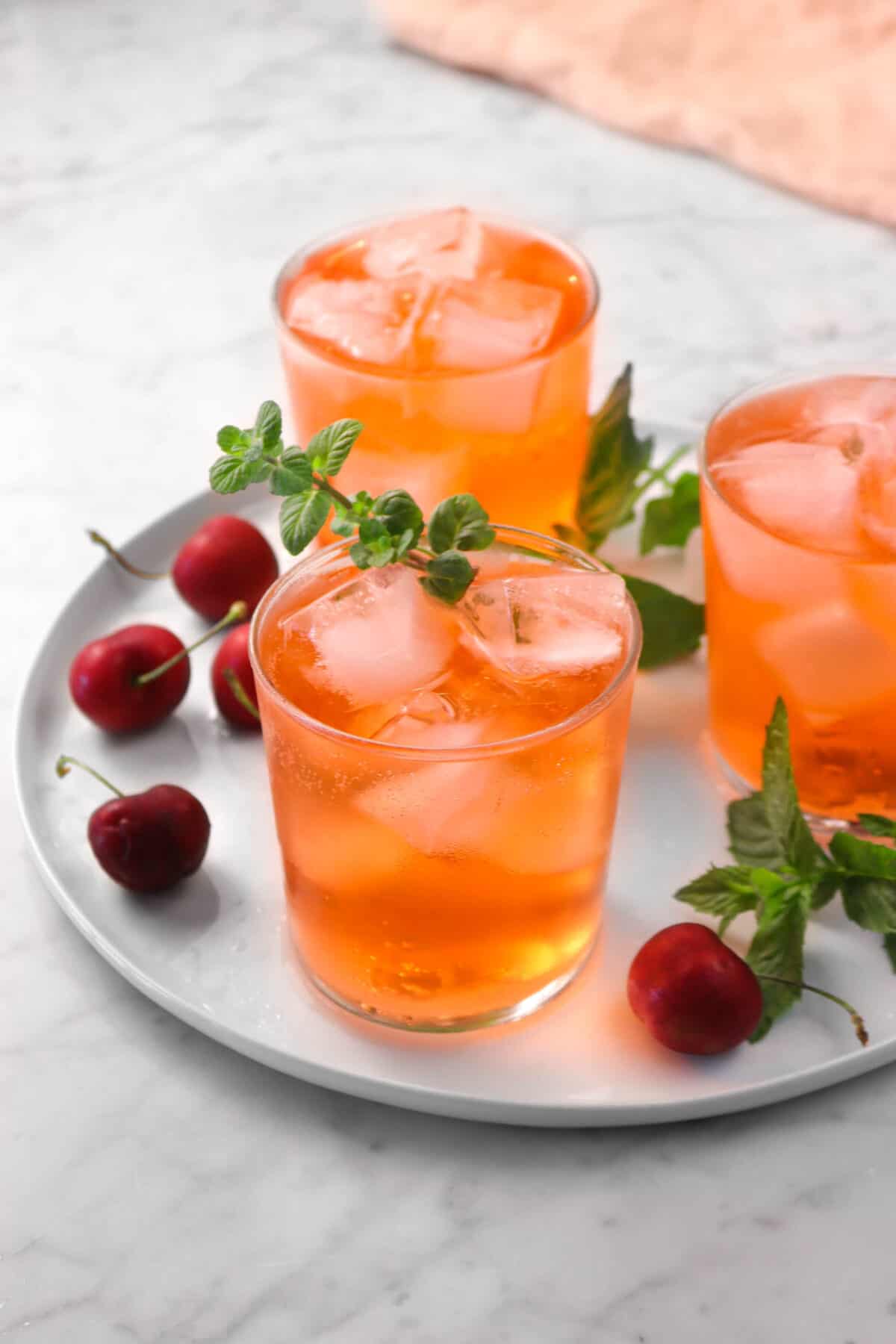 three glasses of Shirley temples on a white plate with cherries, mint, and a pink napkin