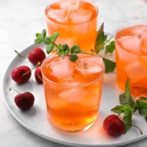 three glasses of Shirley temples on a white plate with cherries, mint, and a pink napkin