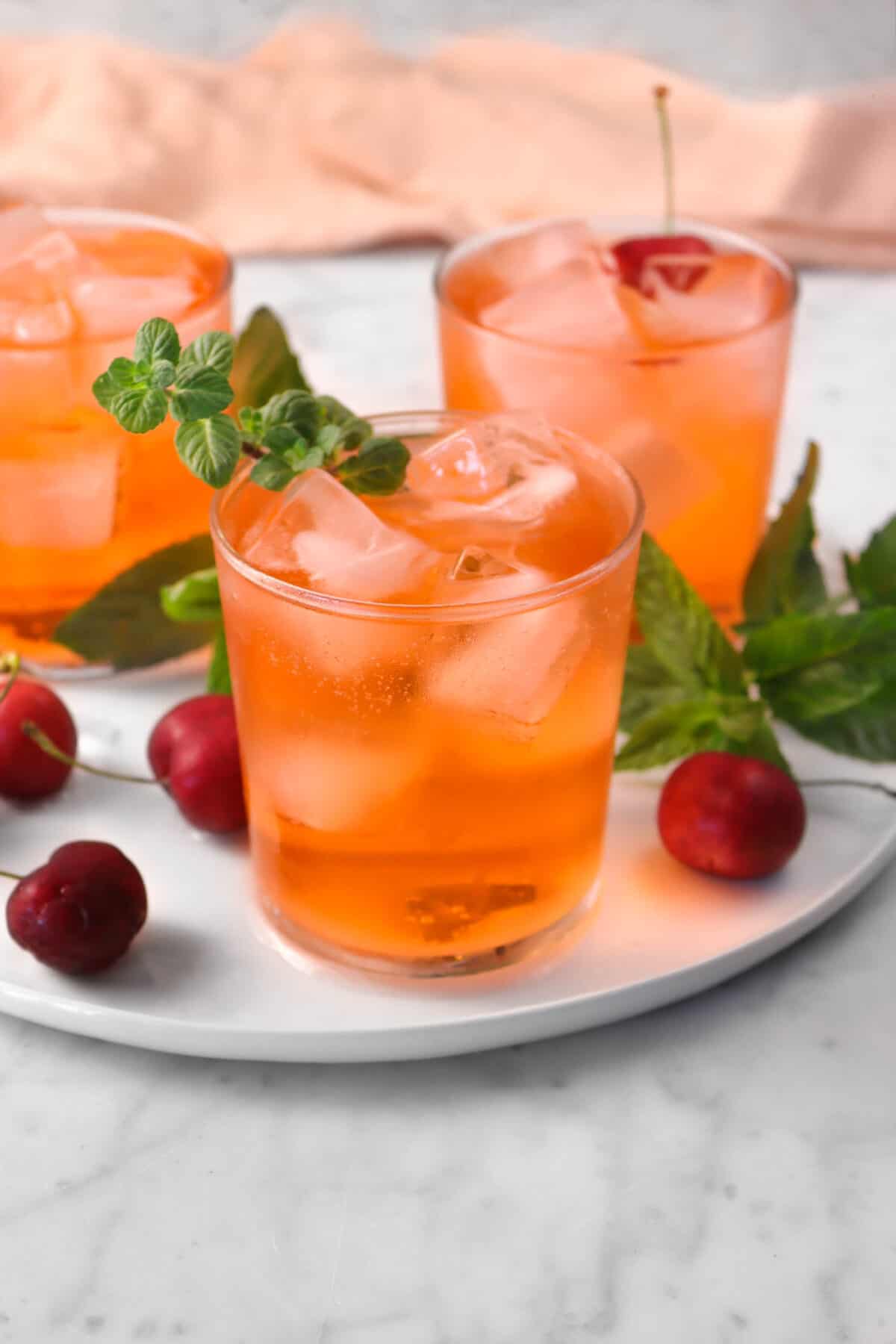 shirley temples on a plate with mint and cherries on a marble counter and a pink napkin