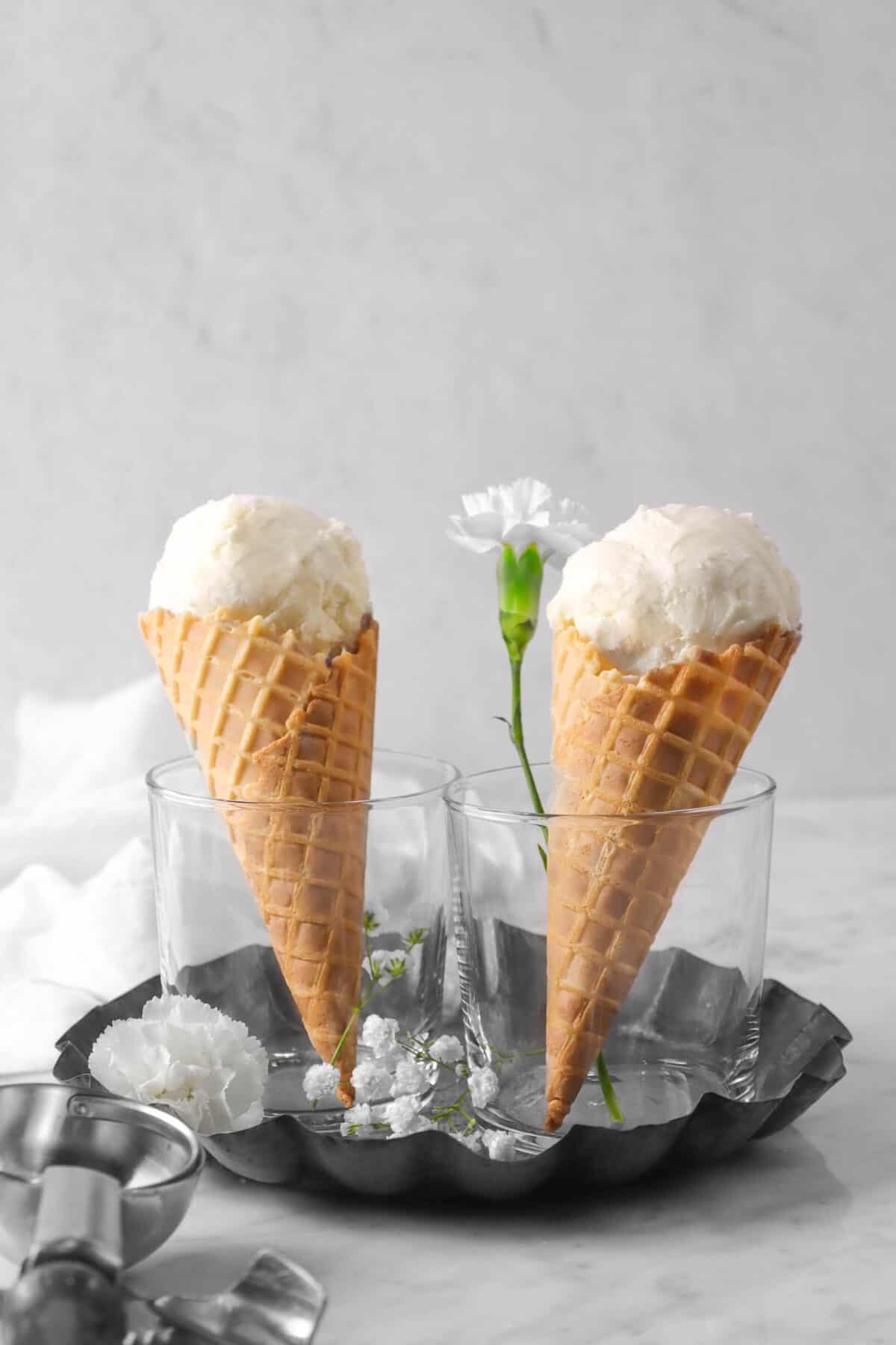 two scoops of vanilla ice cream on two cones with flowers, ice cream scoop, on a pie pan, with napkin