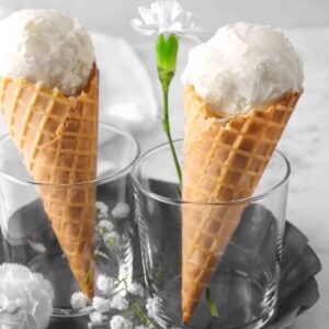 two vanilla ice cream cones with flowers, in glasses, in a pie pan