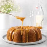 apple cinnamon cake on a white plate with caramel being drizzled onto it