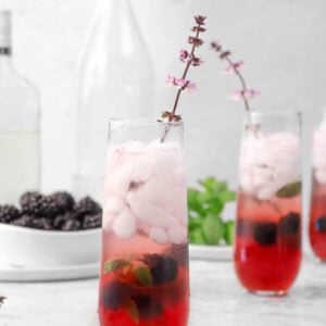 three mojitos with purple flowers, blackberries, two jars, and mint