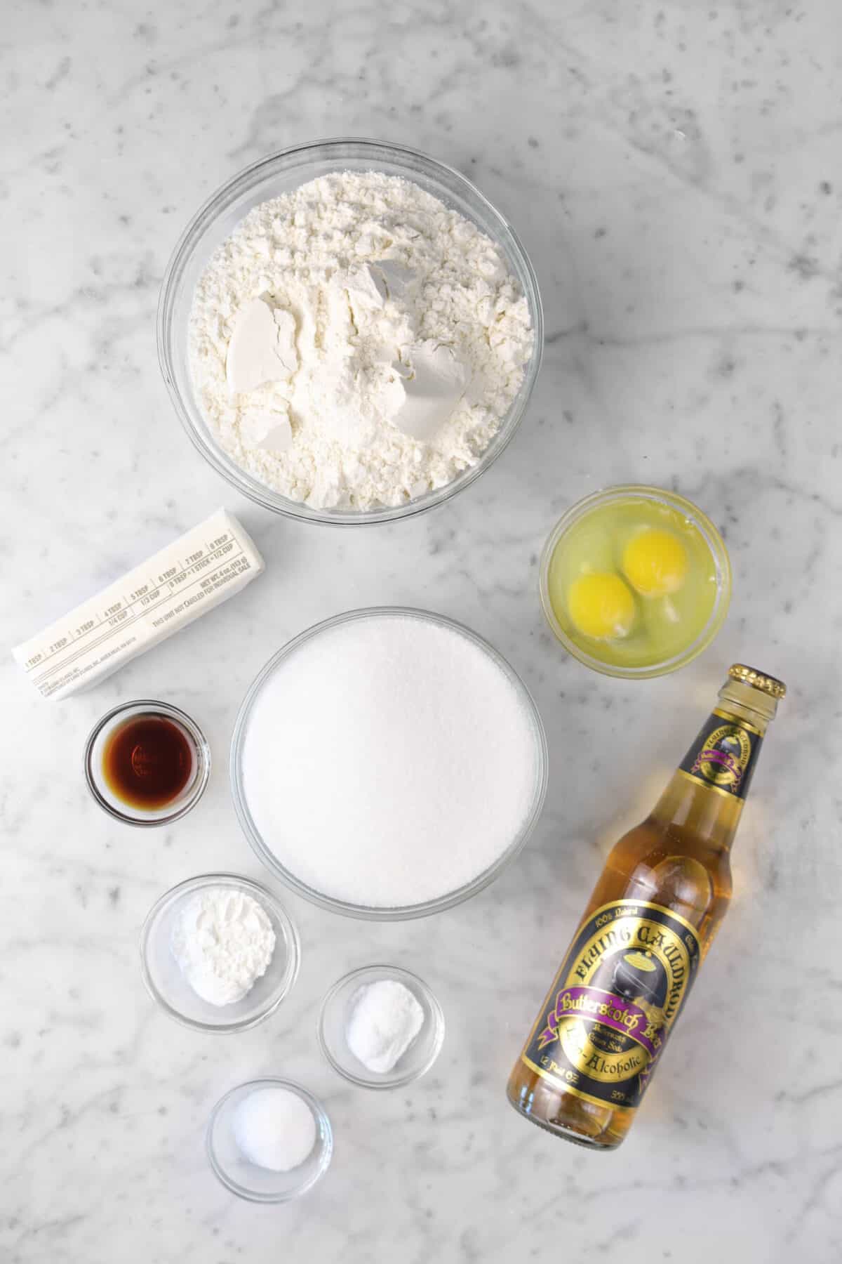 flour, butter, vanilla, sugar, baking powder, baking soda, salt, butterbeer, and eggs on marble counter