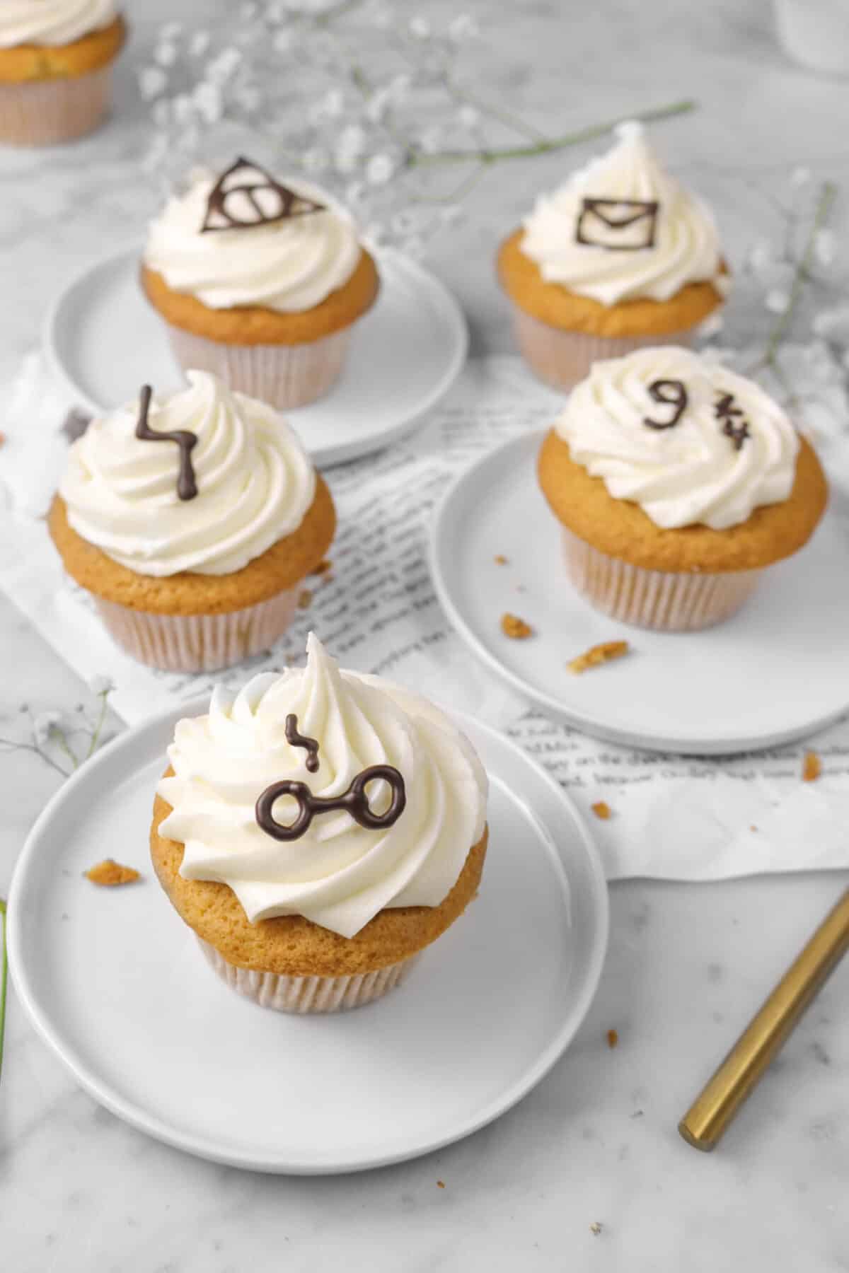 five cupcakes with three on plates sitting on book pages with flowers