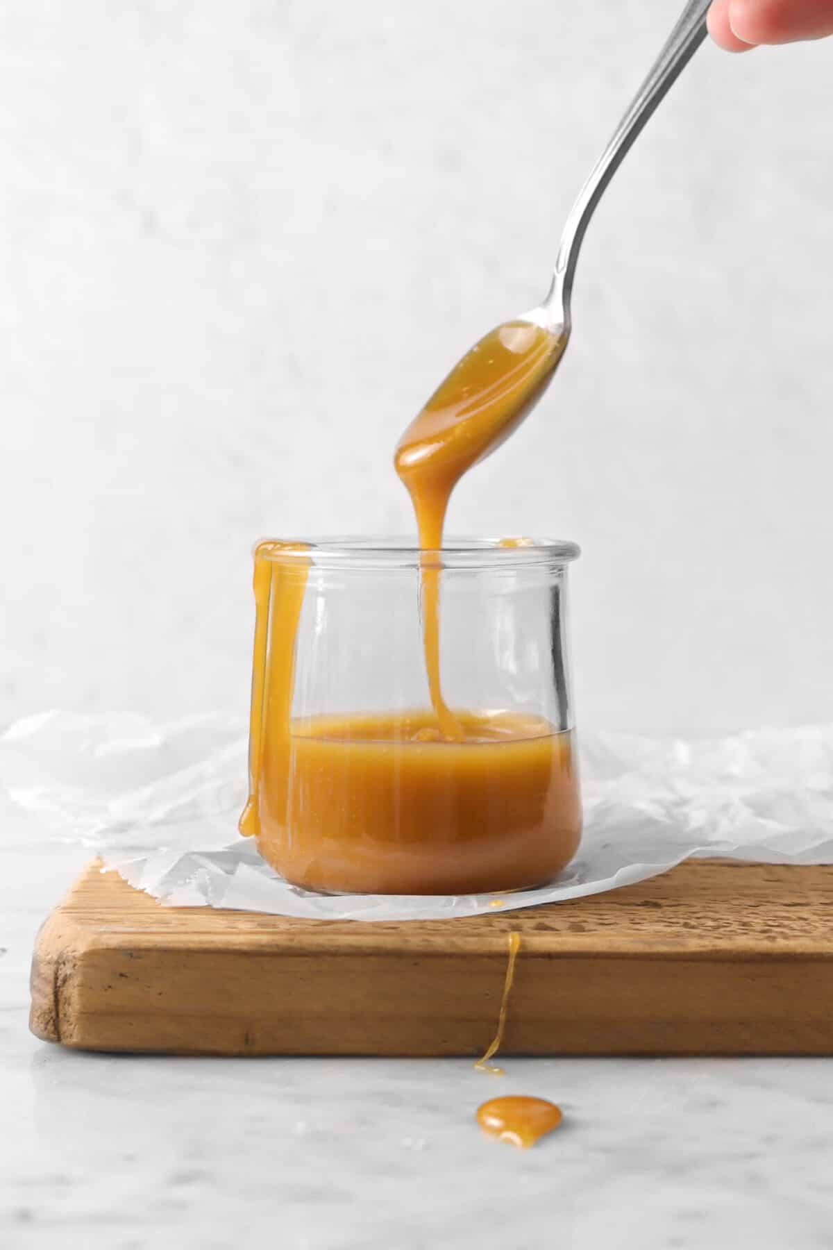 a spoon with caramel sauce running off it into a jar