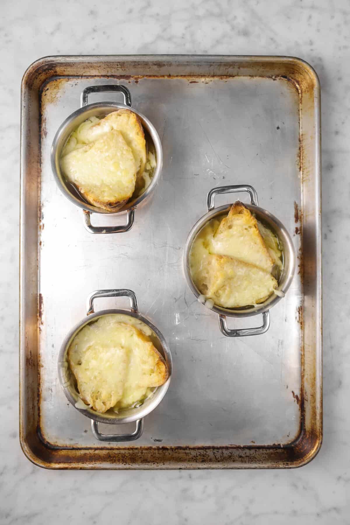three pots of french onion soup on a sheet pan