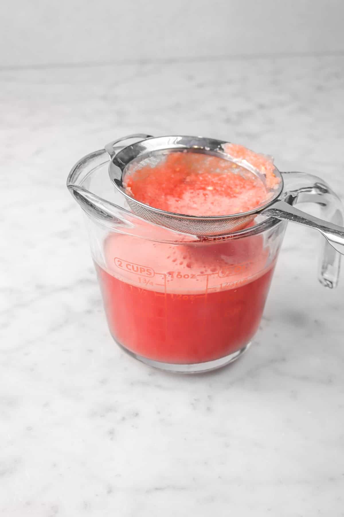 watermelon juice being strained into a cup measure