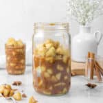 apple pie filling in two jars with a spoon, spices, and flowers