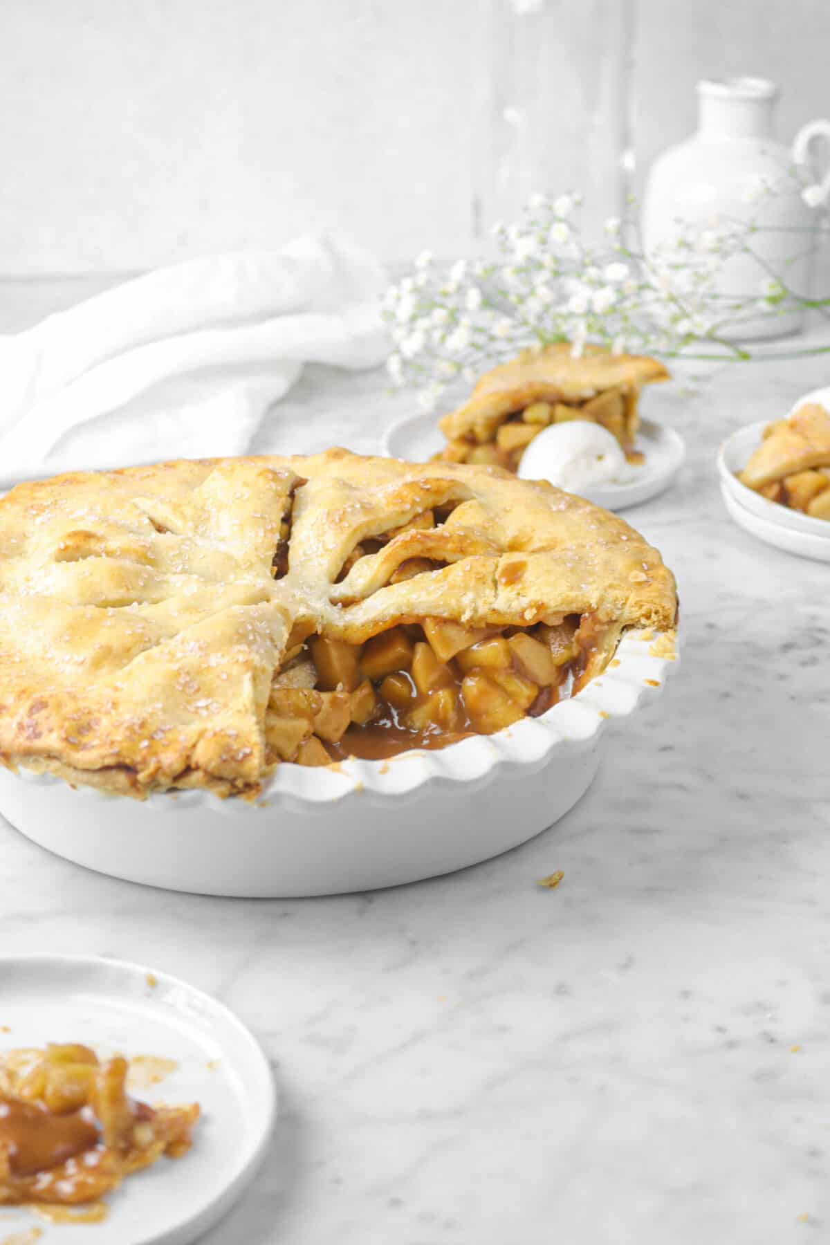 apple pie with two slices behind with flowers and white napkin
