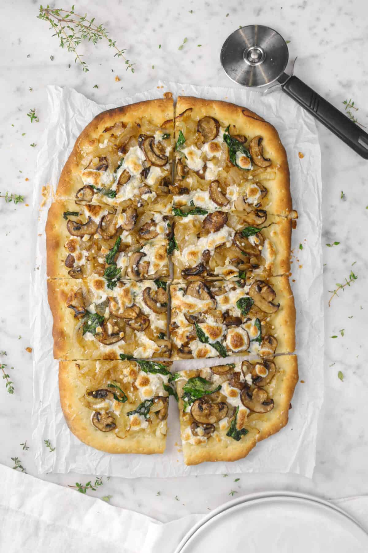 mushroom and spinach flatbread on marble counter with thyme sprigs and pizza cutter