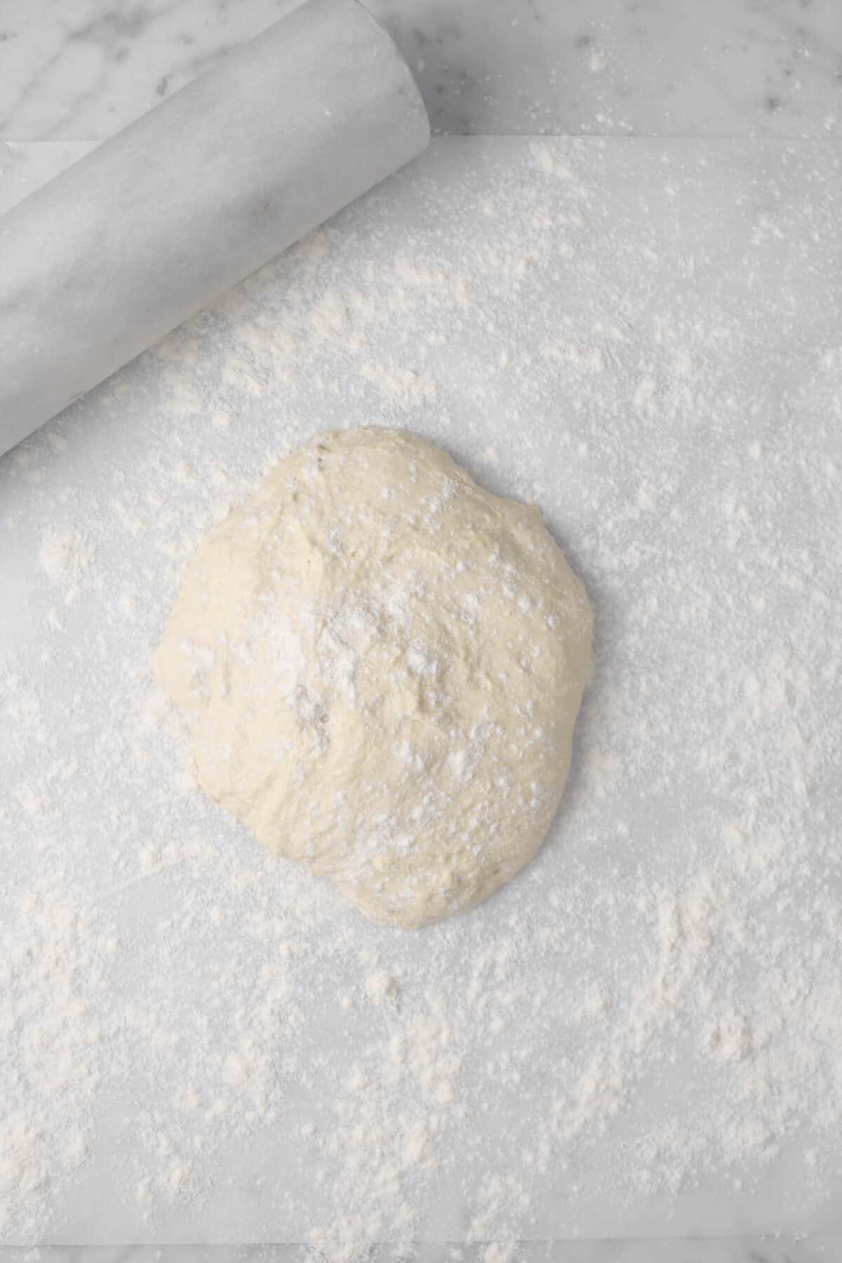pizza dough on floured parchment with marble rolling pin