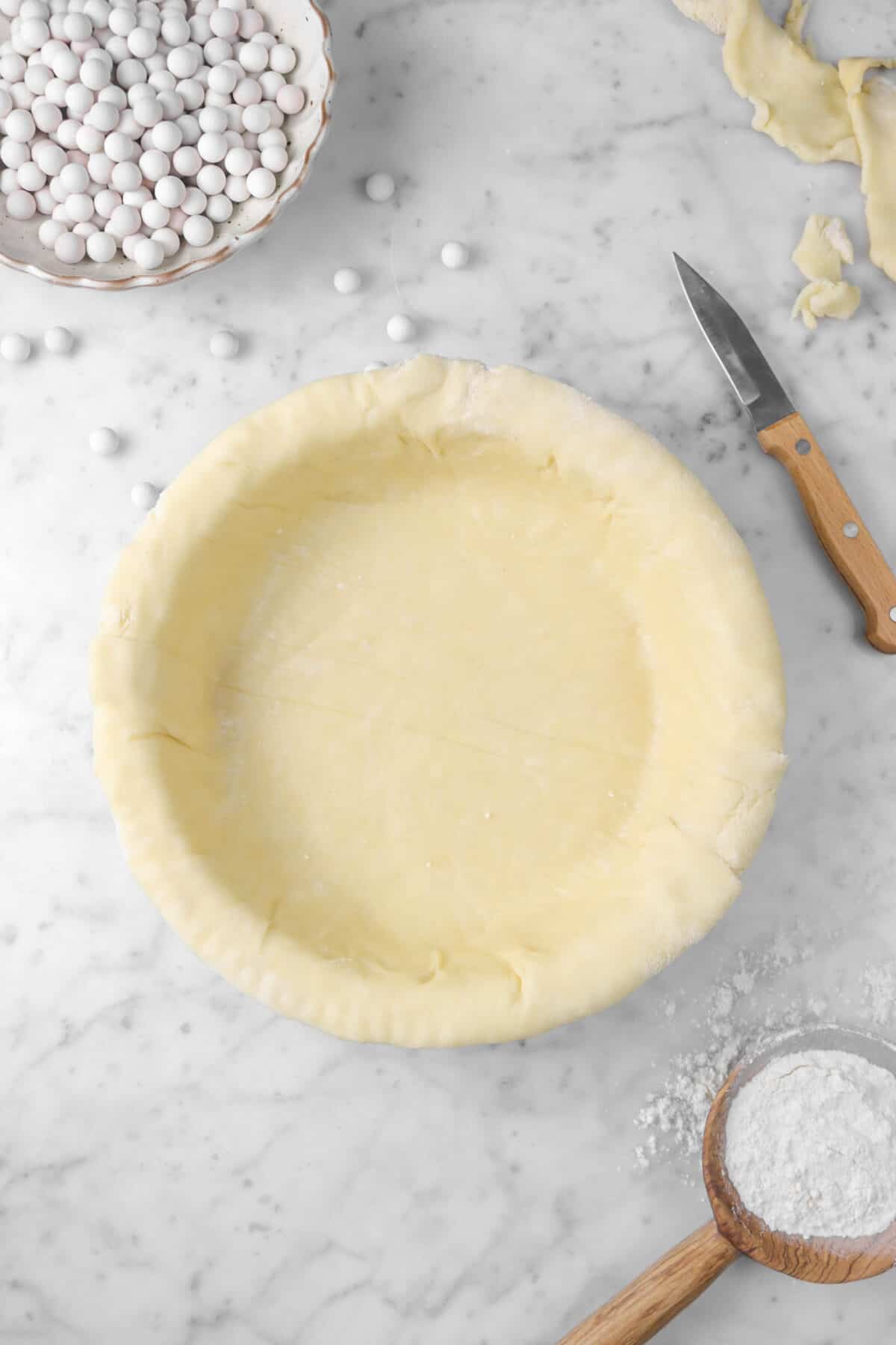 pie dough with pie weights, knife, and flour