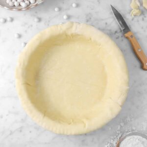 pie dough with pie weights, knife, and flour