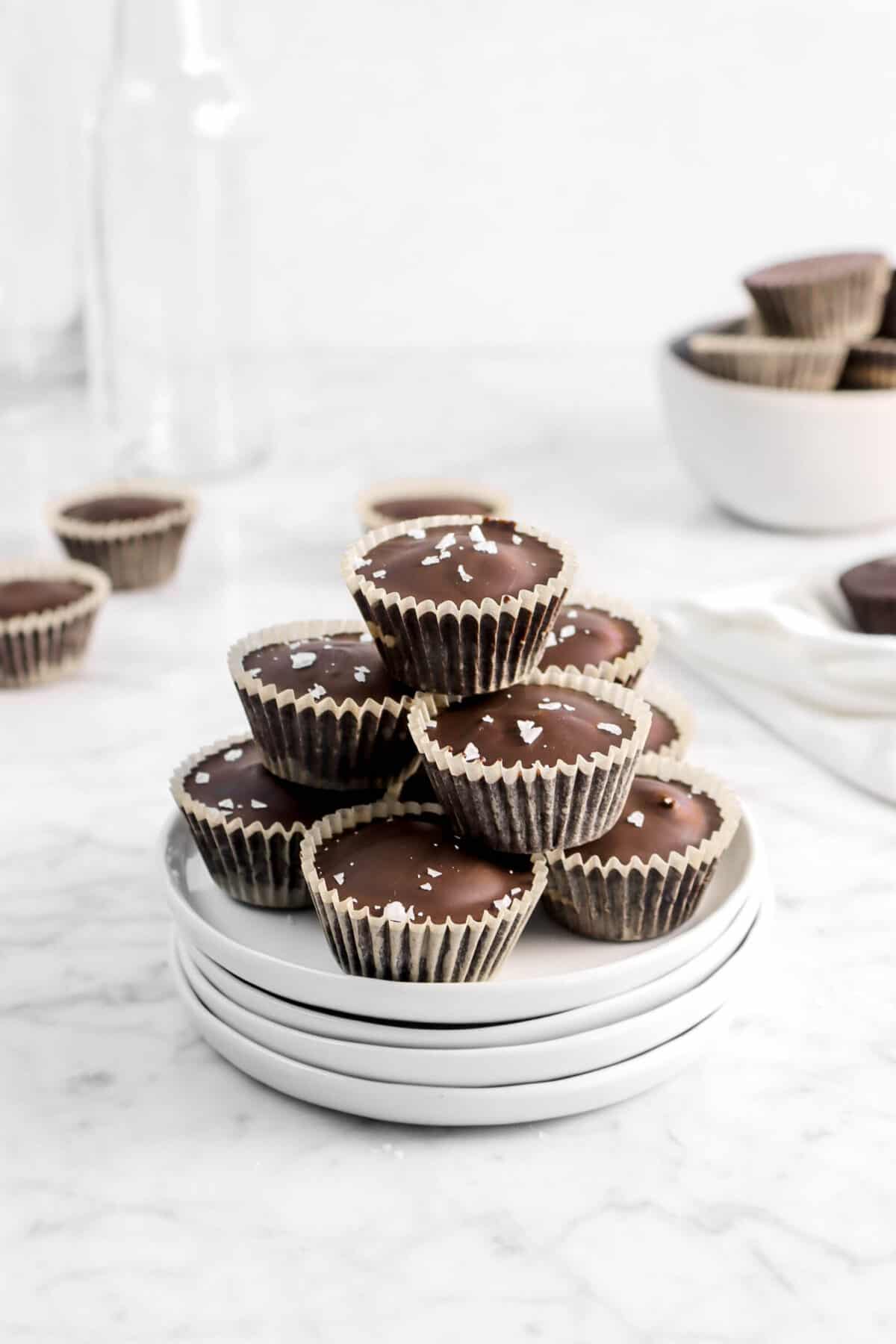 chocolate peanut butter cups stacked on white plates with more chocolates behind