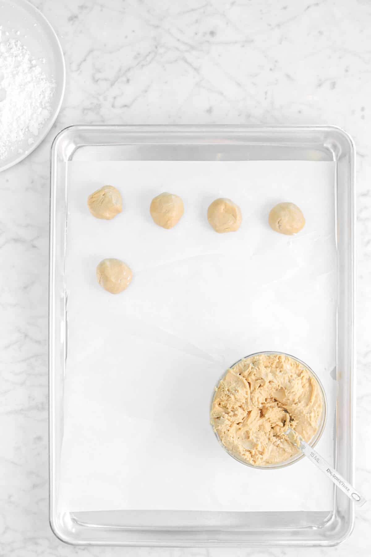peanut butter filling in a small bowl with five balls rolled on a sheet pan