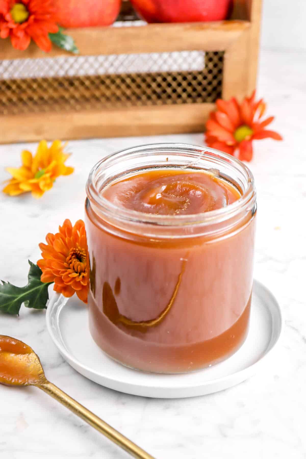 apple butter in a glass jar on a white plate with flowers
