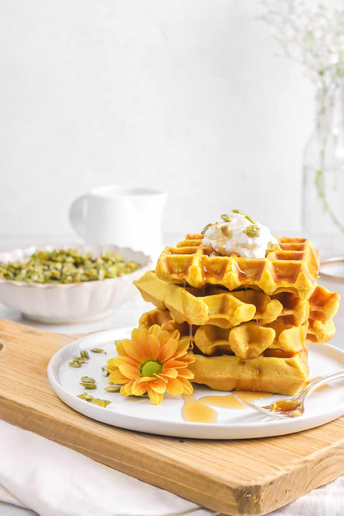 waffles stacked with maple syrup dripping, candied pepitas, with whipped cream on top, and flowers