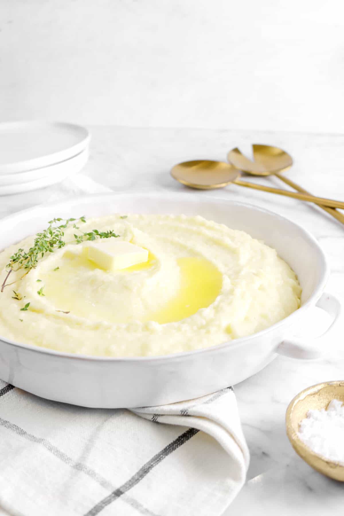 mashed potatoes with melted butter, thyme leaves on top with plates and serving spoons behind