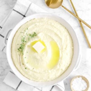 mashed potatoes in white palte with butter, thyme, a napkin, salt, and serving spoons