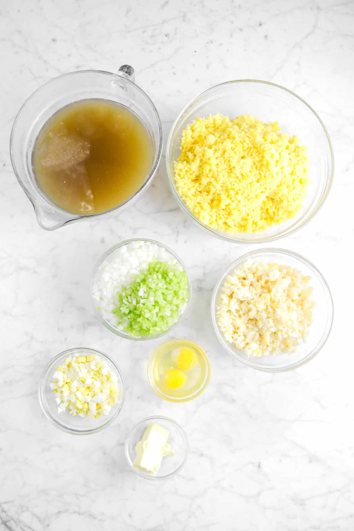 chicken stock, cornbread crumbles, onion, celery, chopped biscuits, two eggs, chopped boiled egg, and butter in glass bowls