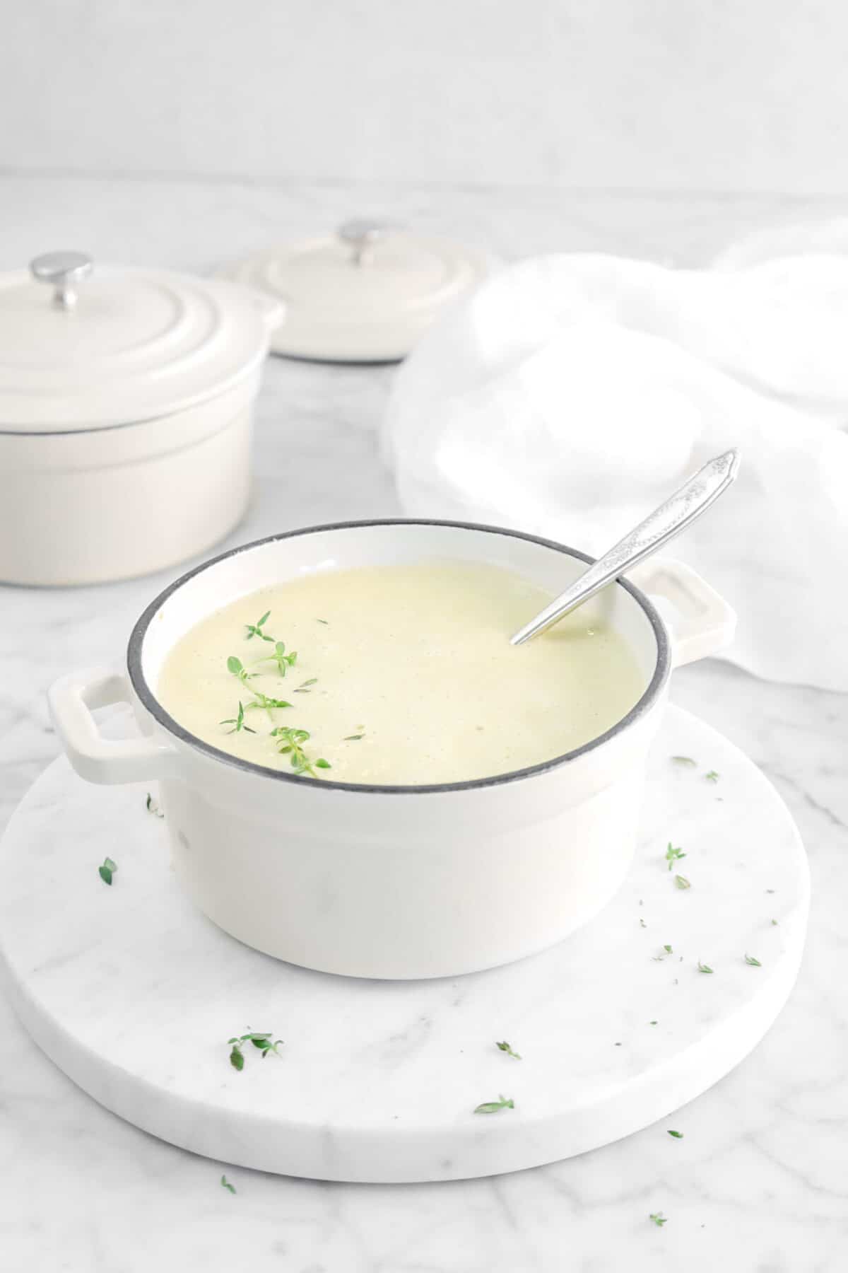 cream of celery soup in a small pot with a spoon and fresh thyme