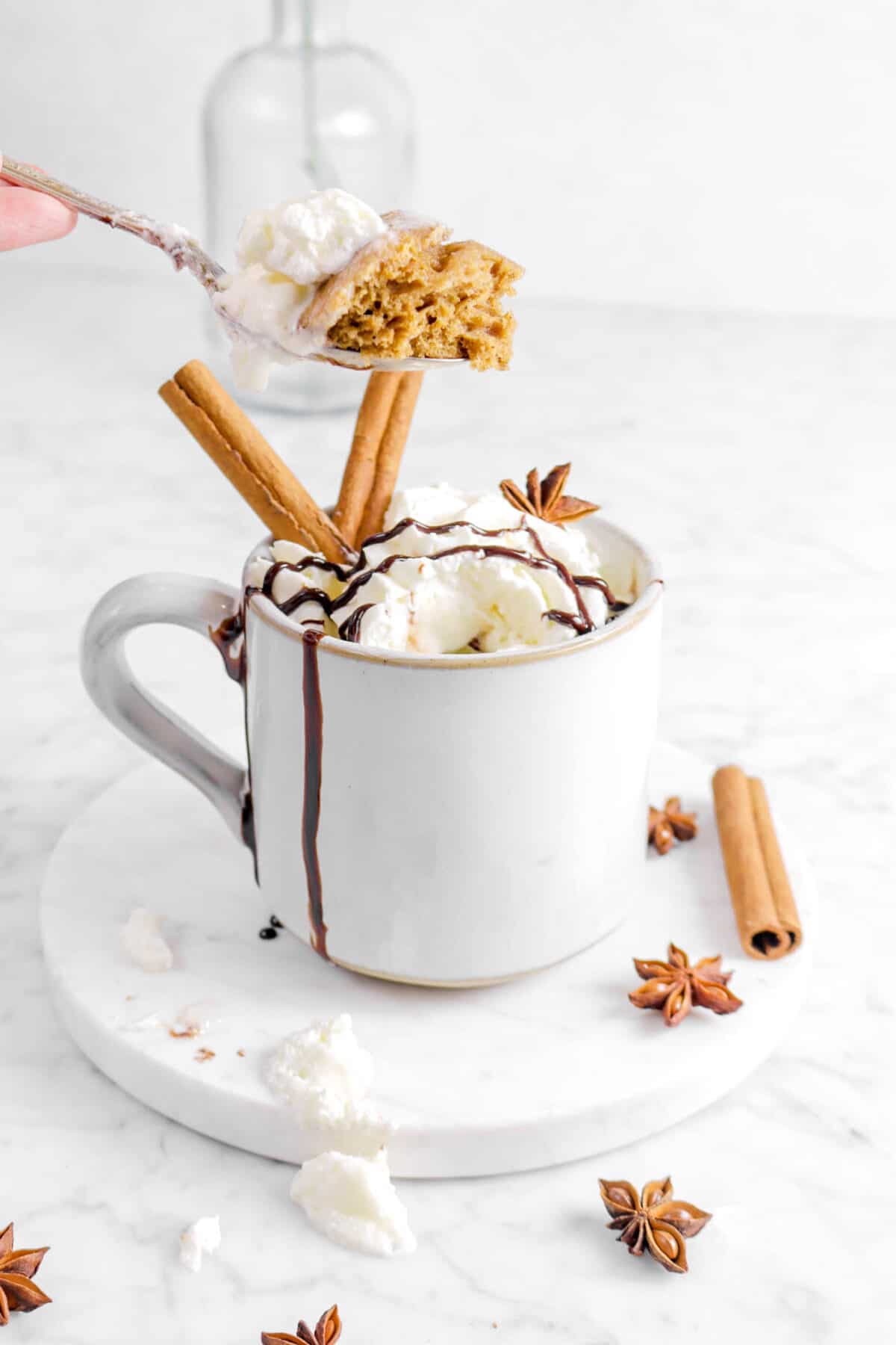 spoon held above mug with cake and whipped cream