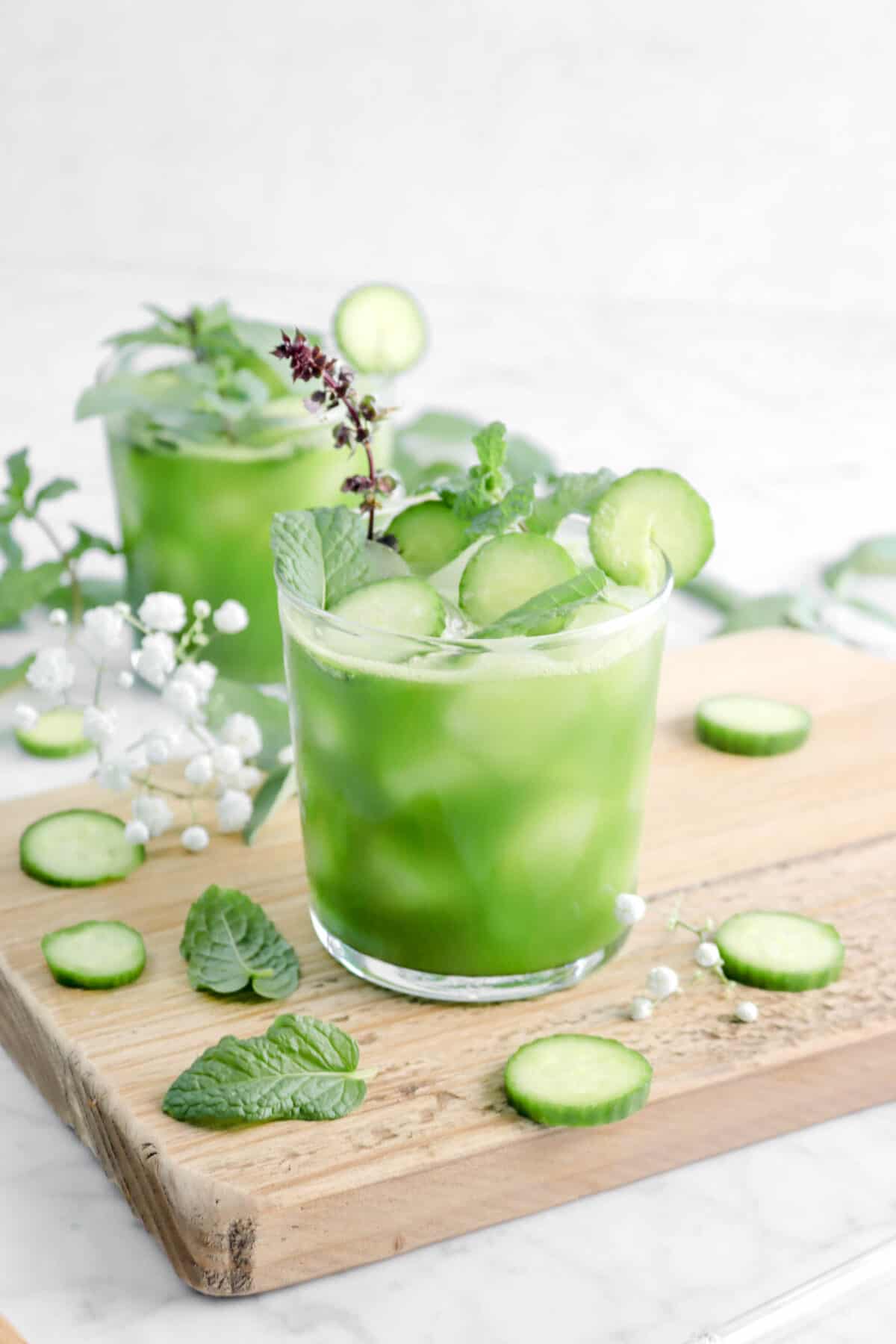 two glasses of green juice with cucumber slices, mint leaves, and flowers