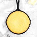 cornbread in cast iron skillet with butter, honey, salt, and a napkin