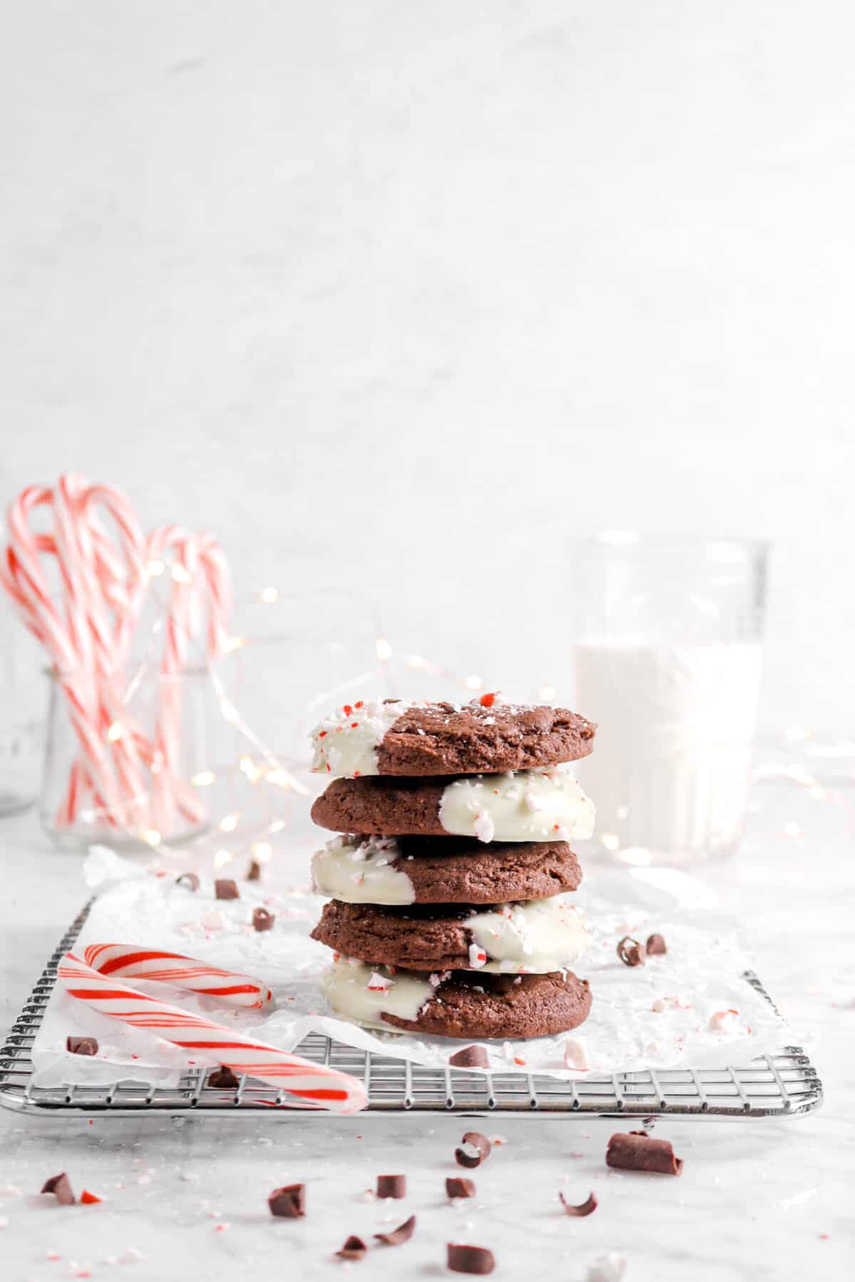 five peppermint cookies stacked on wite cooling rack with candy canes and glass of milk behind