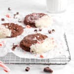 three chocolate peppermint cookies on wire cooling rack with glass of milk behind, chocolate curls, and crushed peppmint