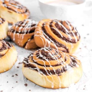 six chocolate sweet rolls on parchment with mug of coffee behind