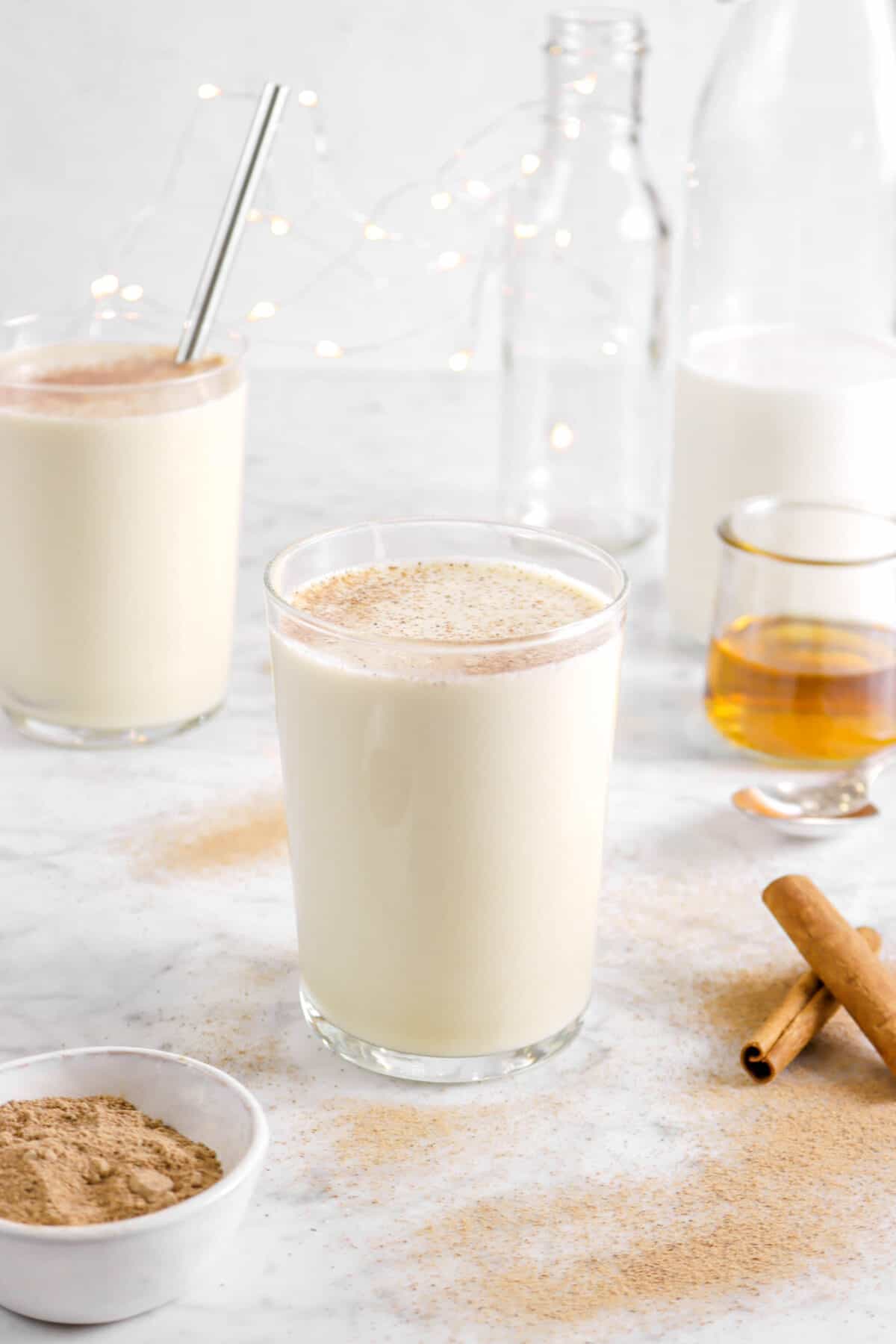 eggnog in two glasses with nutmeg on top with milk, bourbon, and cinnamon sticks