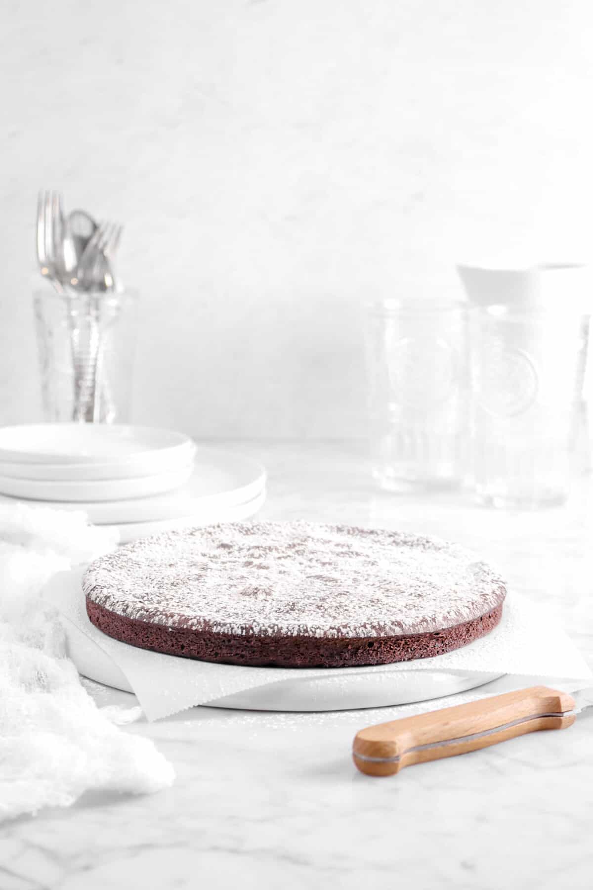powdered sugar on top of cake with white cheese cloth, a knife, and two glasses