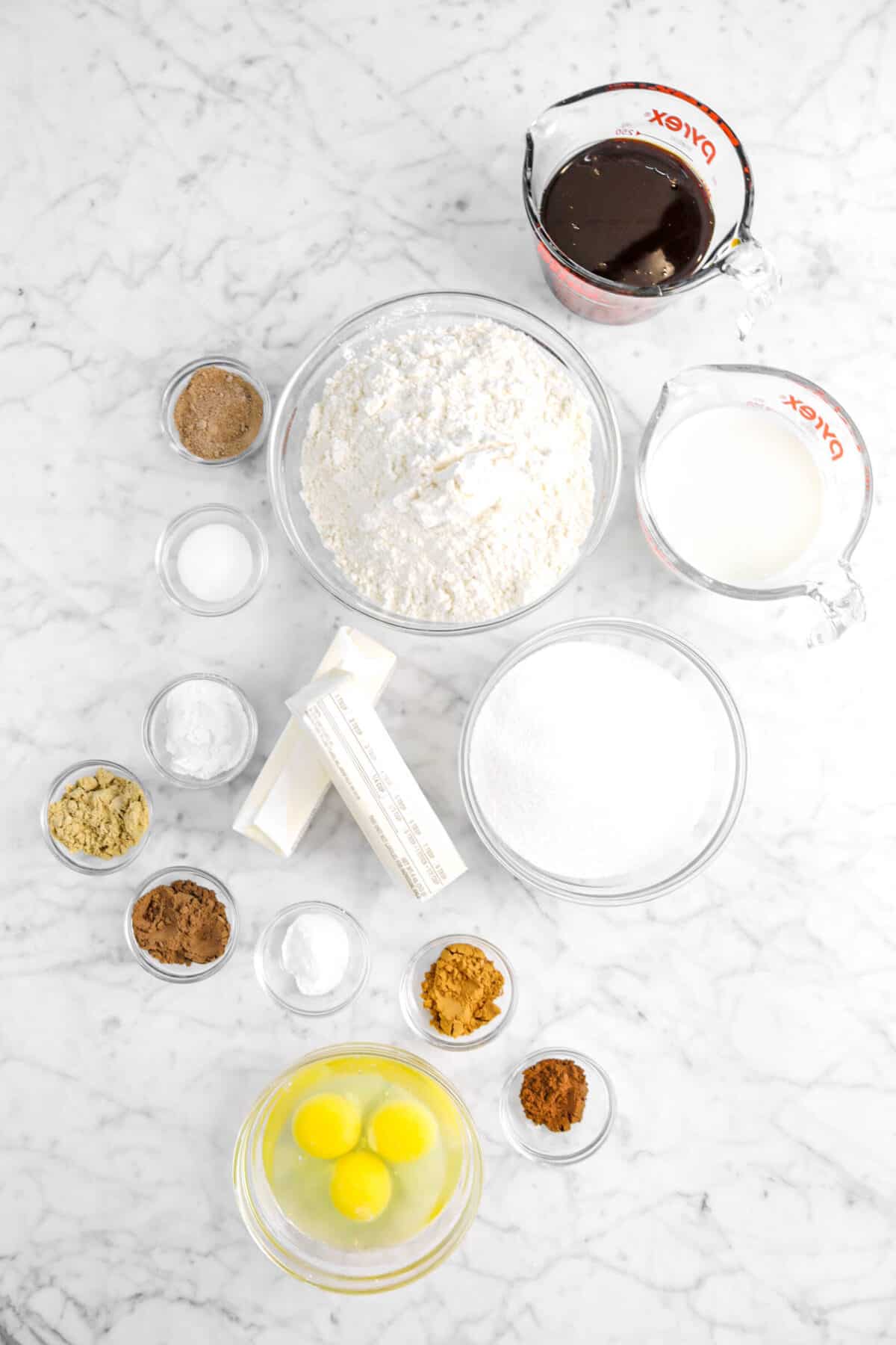 molasses, flour, nutmeg, salt, baking power, ginger, all spice, baking powder, cinnamon, cloves, butter, sugar, milk, and eggs on a marble counter
