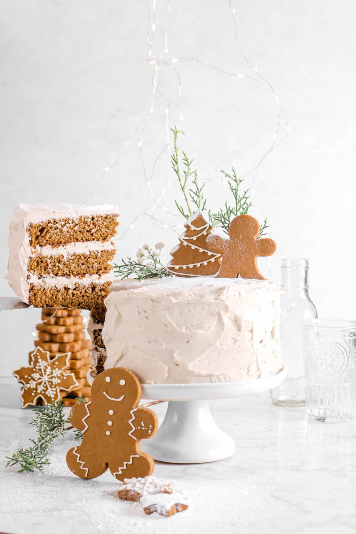 cake slice being pulled away from cake with gingerbread cookies, greenery, and glasses