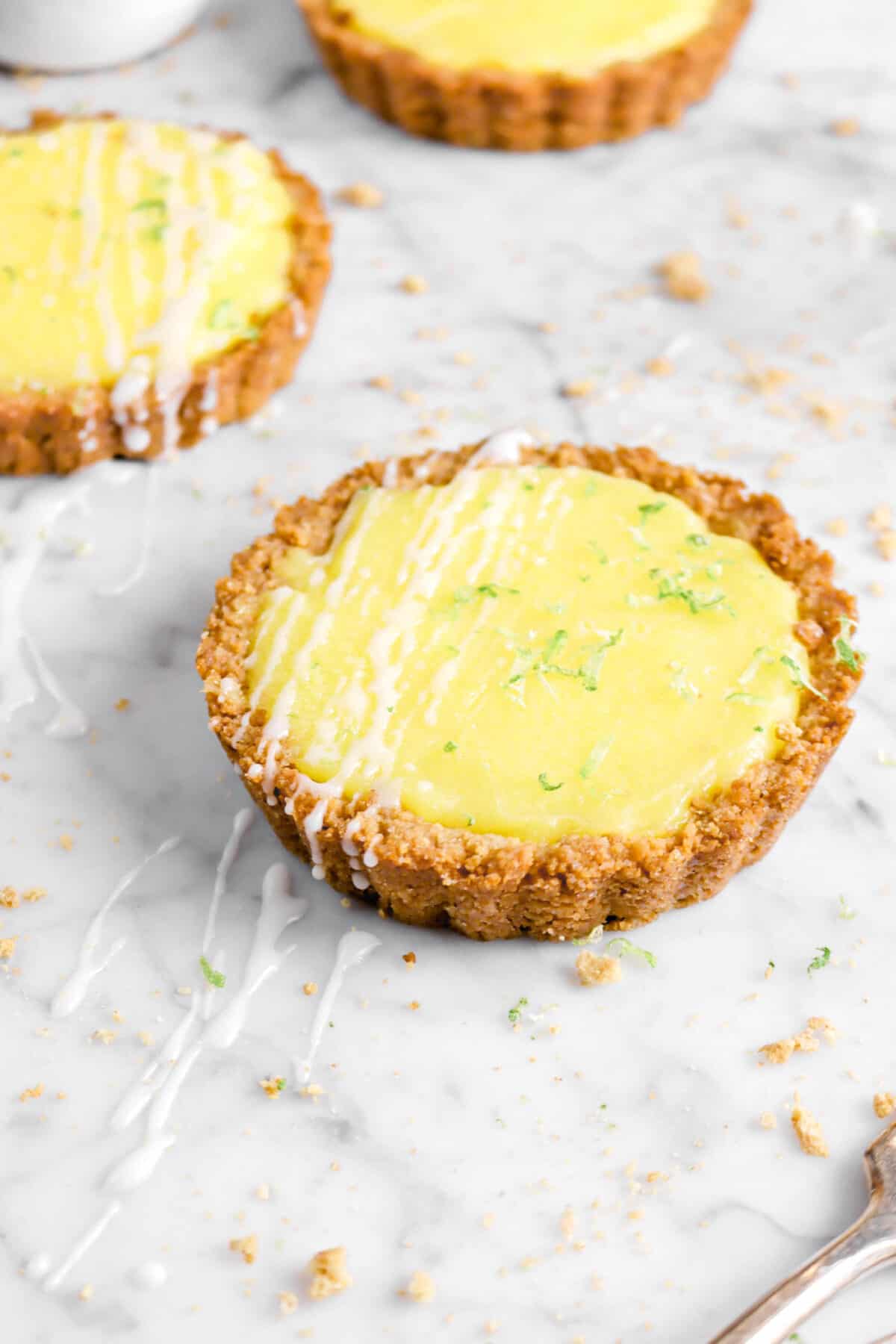 key lime pies on marble counter with zest, drizzle, and crumbs