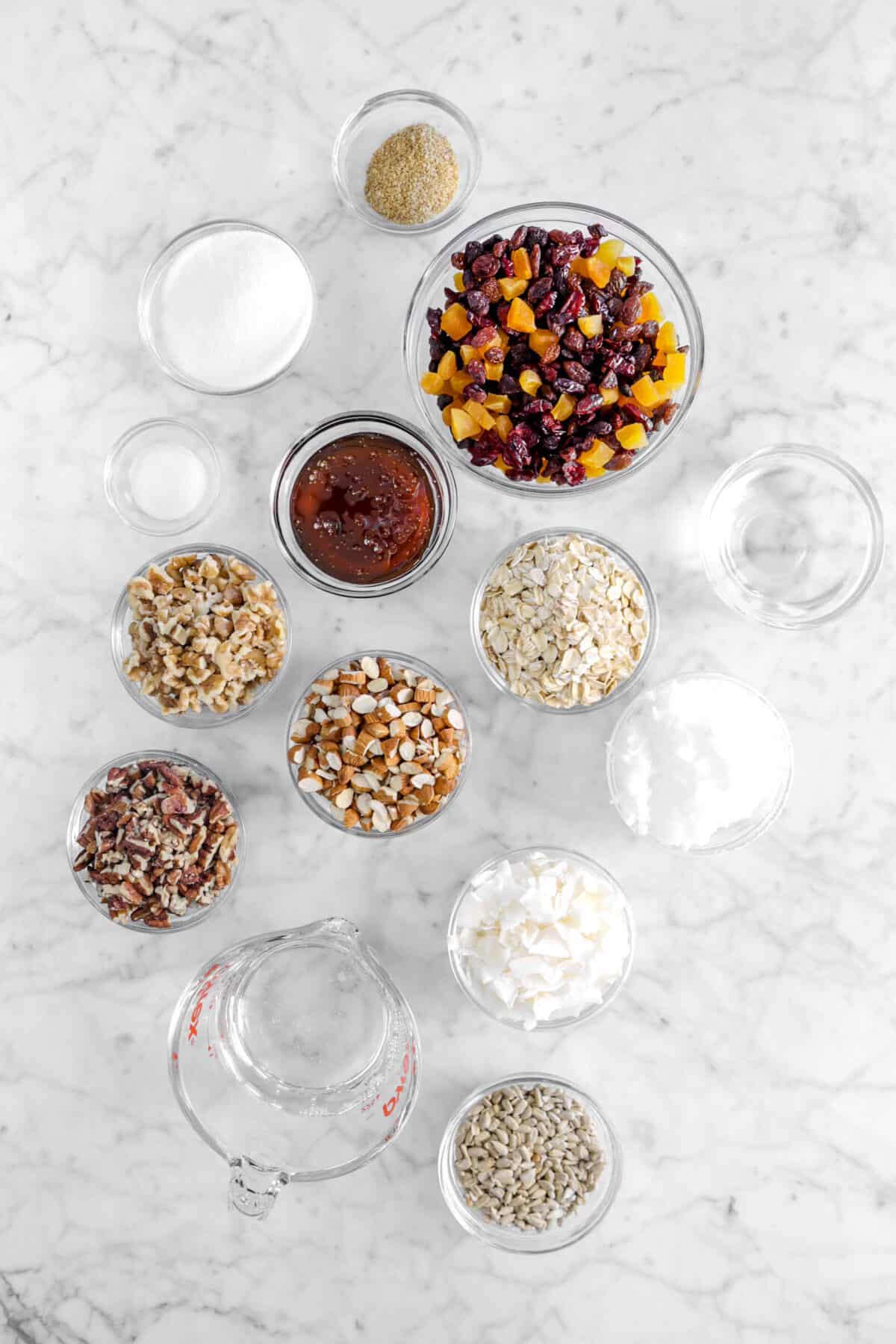 wheat germ, chopped fruit sugar, salt, honey, chopped walnuts, almonds, pecans, oatmeal, water, coconut oil, coconut flakes, water, corn syrup, and pumpkin seeds in glass bowls