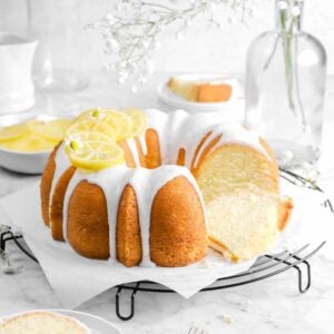 bundt cake on wire cooling rack with flowers, a slice in front, slice behind, and candied lemon slices