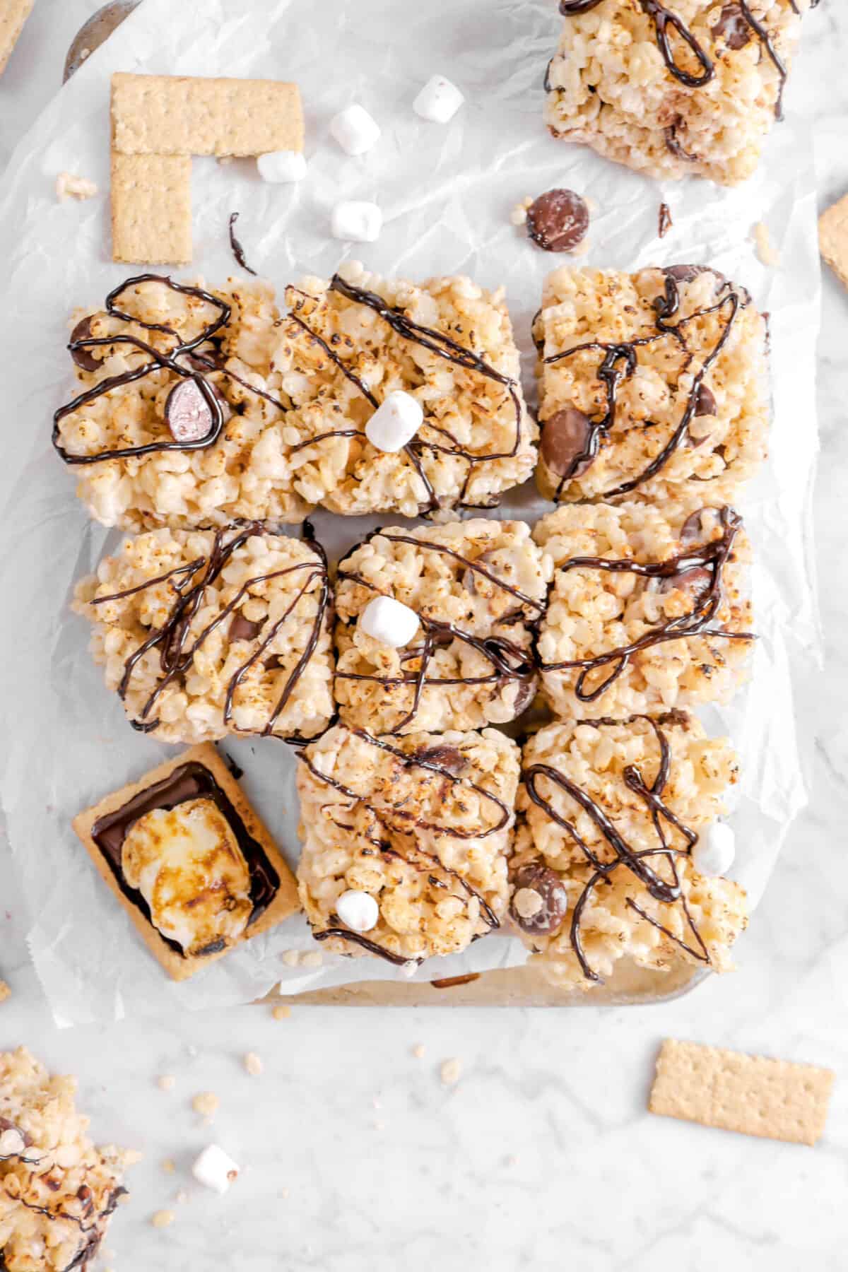 eight rice krispie treats on parchment with a s'more, graham cracmers, mini marshmallows, and more krispie treats