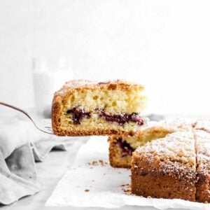 blueberry coffee cake slice being held over coffee cake on parchment paper