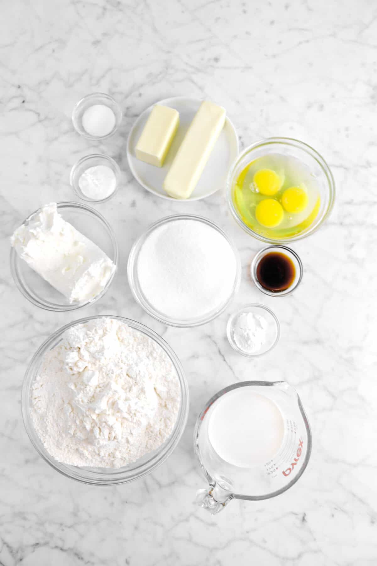 salt, baking powder, baking soda, butter, sugar, eggs, vanilla, cream cheese flour, and milk on marble counter