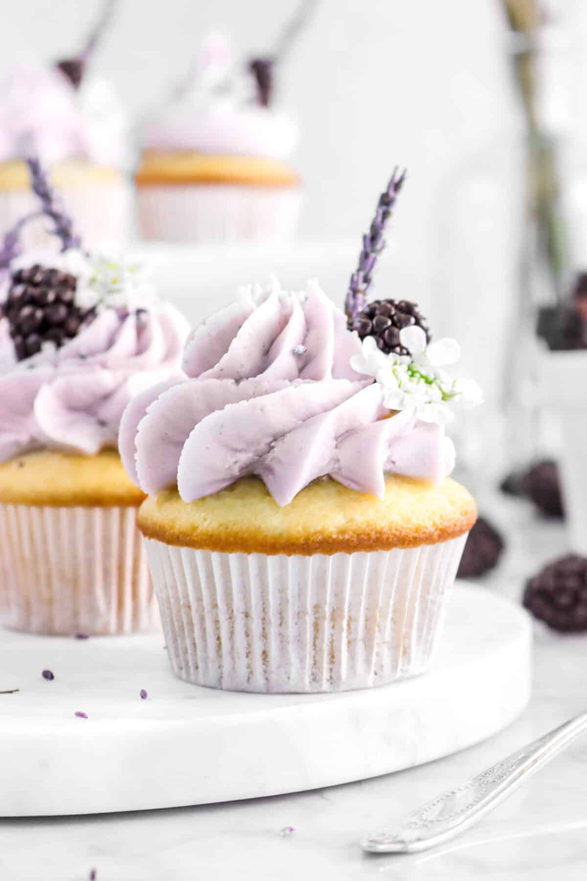 close up of blackberry lavender cupcake with a piece of lavender, a blackberry, and flower on the frosting