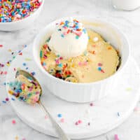 funfetti cake in white ramekin with a spoonful of cake on marble board with ice cream and sprinkles