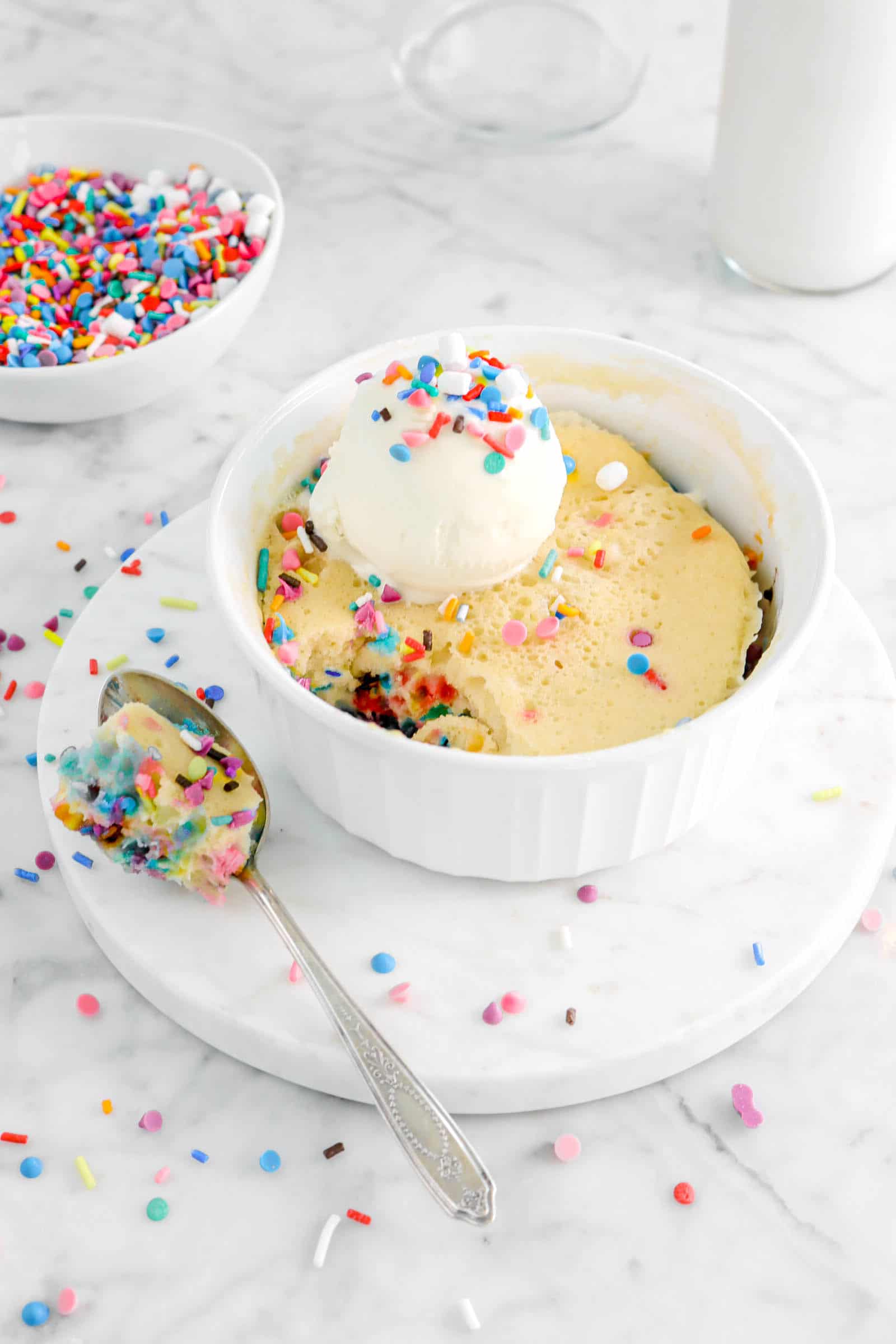 funfetti cake in white ramekin with a spoonful of cake on marble board with ice cream and sprinkles