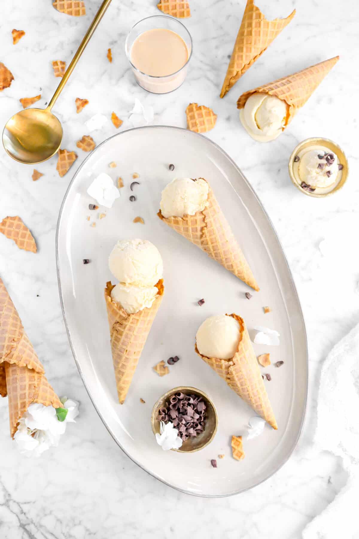 three cones of irish cream ice cream on server with cones around, chocolate curls, gold spoon, and gold bowl of ice cream