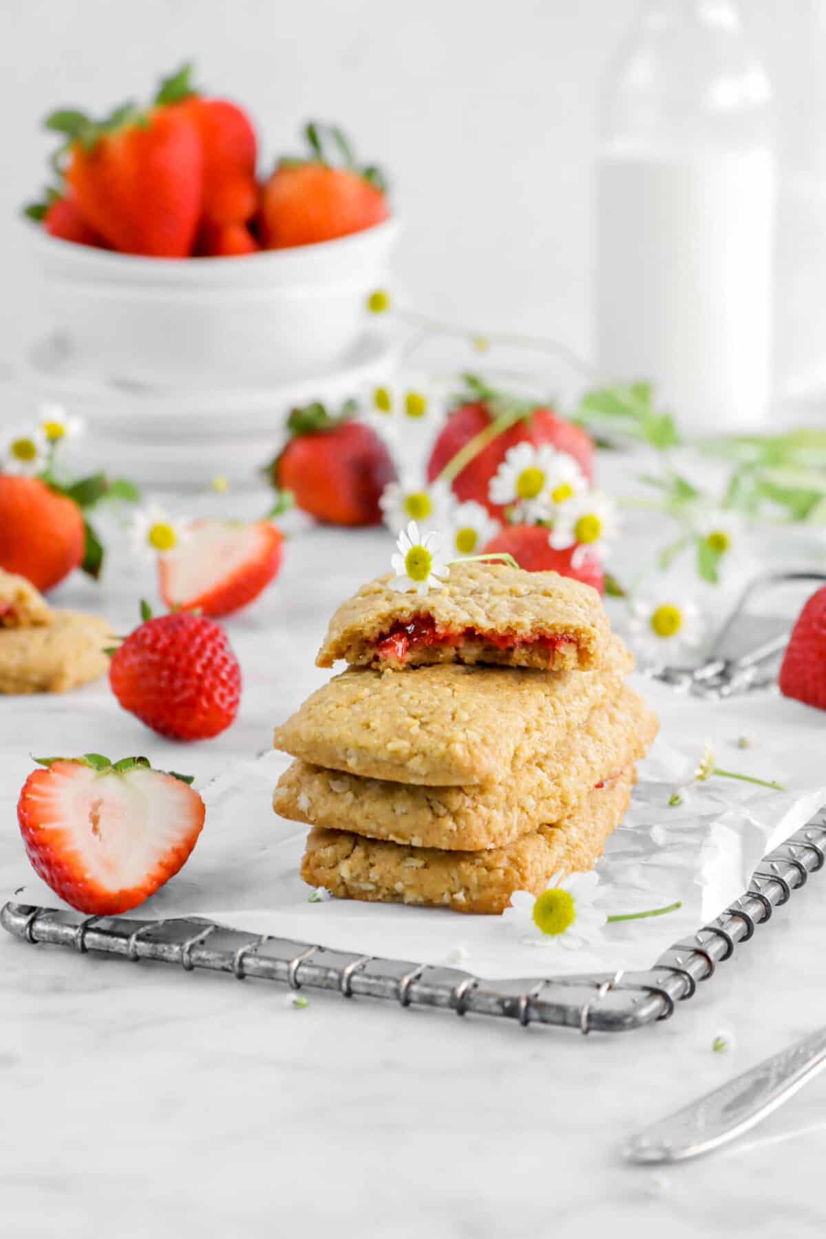 four stacked strawberry nutri grain bars with chamomile flowers, strawberries, and glass of milk behind